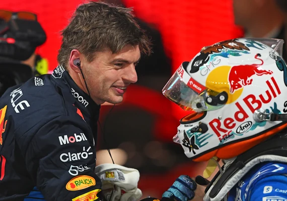 Max Verstappen in Red Bull racing gear speaking with another driver after a race.