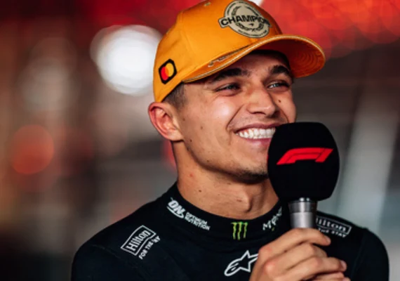 Lando Norris smiling with an F1 microphone and an orange championship cap.